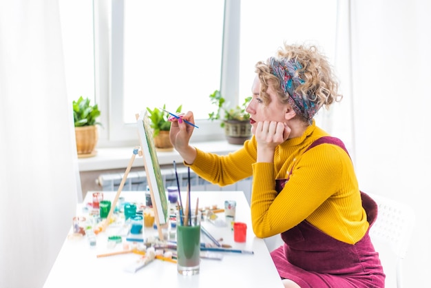 A student artist meticulously crafting a greeting card design at their desk, surrounded by art supplies and colorful sketches, with a focused expression.