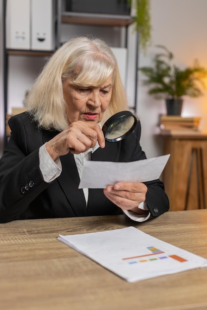A person using a magnifying glass to examine a document with financial charts and graphs, symbolizing the research and investigation required to find unclaimed retirement benefits.