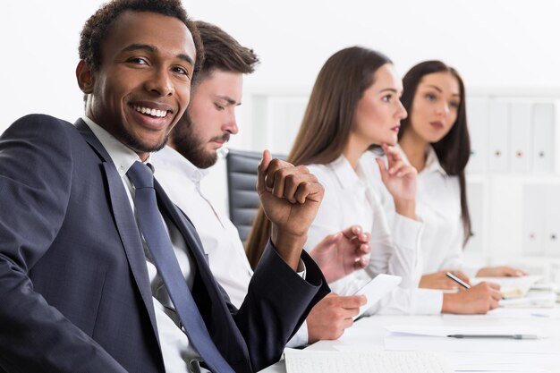 A diverse group of people looking at a financial advisor who is pointing to a chart illustrating retirement savings growth. They are in a modern office setting, emphasizing the importance of financial planning.
